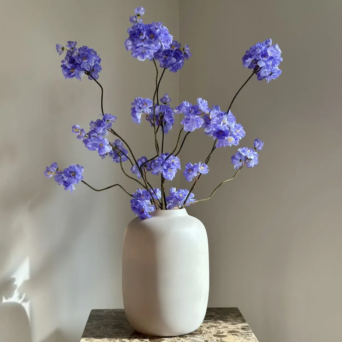 Beige vaas mat met blauw paars zijden bloesemtakken