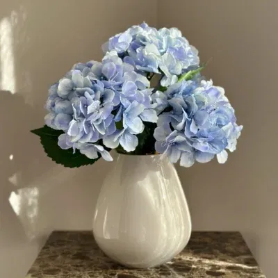 Beige vaas met blauwe kunst bloemen boeket